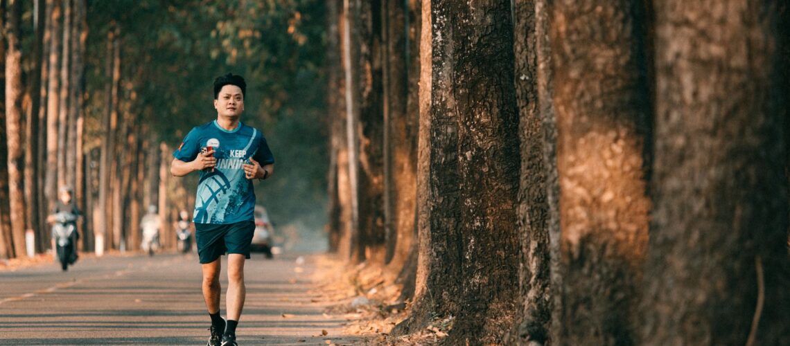 An athletic man runs along a picturesque tree-lined street during autumn. Perfect for fitness and outdoor themes.