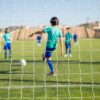 Group of children playing soccer on a sunny day in Portugal, seen through the goal net.
