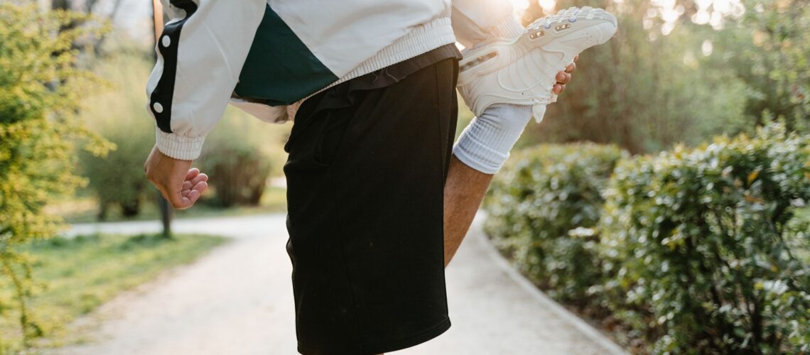 Close-up of a person stretching leg in a sunny outdoor park, ideal for fitness themes.