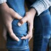 Close-up image of hands holding a knee in jeans, indicating pain or injury.