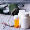Close-up of medical supplies including pill bottles and a blood pressure monitor on a wooden surface.