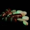 Assorted pills and capsules in green light on dark surface, representing pharmaceuticals.