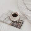 Minimalist morning scene with a cup of coffee and newspaper on a neatly made bed.