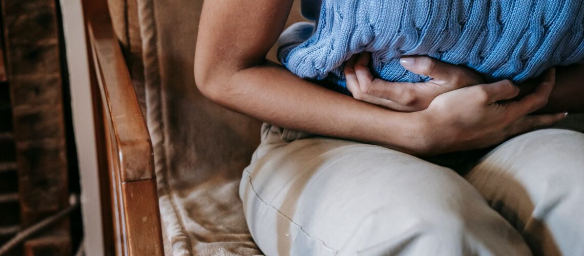 Crop unrecognizable female touching belly while having acute pain in stomach sitting on couch