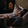 A woman peacefully sleeping with an eye mask in a dimly lit bedroom, capturing a serene bedtime atmosphere.