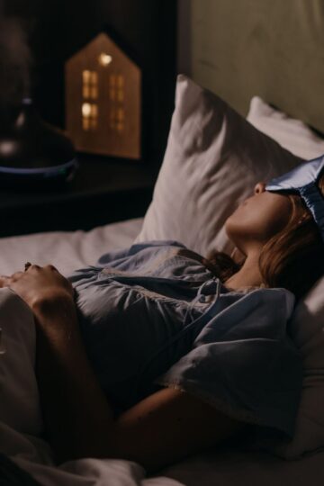 A woman peacefully sleeping with an eye mask in a dimly lit bedroom, capturing a serene bedtime atmosphere.