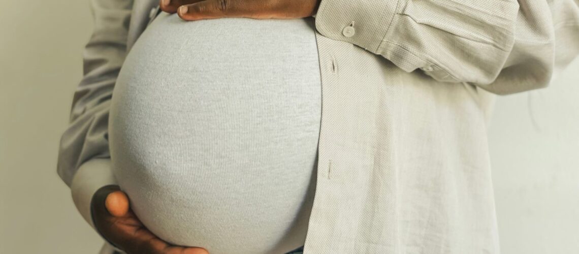 Pregnant woman in casual attire gently holding her belly, symbolizing motherhood.