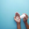 Hands pouring pills from a bottle on a blue background, representing healthcare and medication.