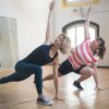 Two women performing yoga poses indoors, symbolizing health and wellness.