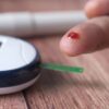 A close-up of a finger prick and blood glucose monitor for diabetes testing.