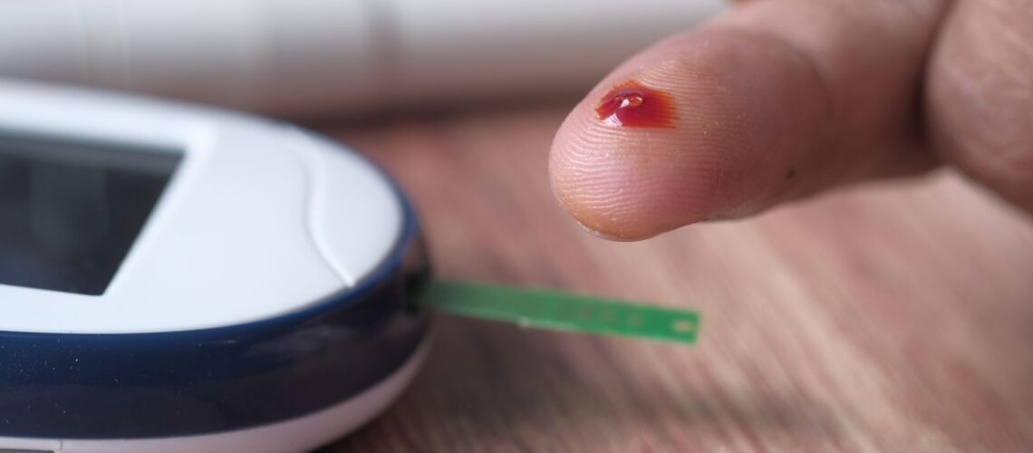 A close-up of a finger prick and blood glucose monitor for diabetes testing.