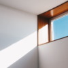 A minimalist interior showcasing sunlight streaming through a modern glass window against a blue sky.