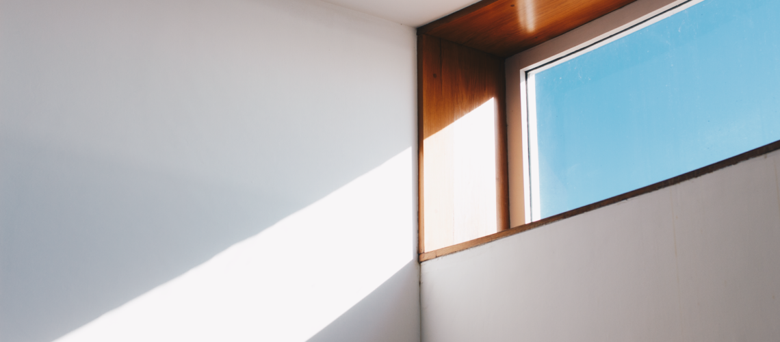 A minimalist interior showcasing sunlight streaming through a modern glass window against a blue sky.