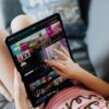 A child using a tablet for streaming cartoons, relaxing on a couch indoors.