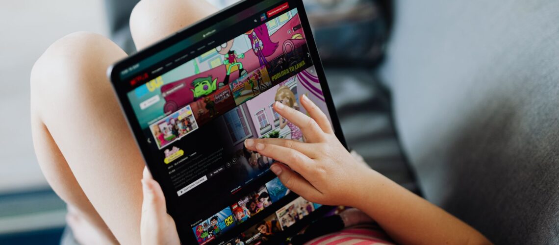 A child using a tablet for streaming cartoons, relaxing on a couch indoors.