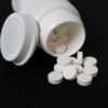 Close-up of white tablets spilling from a plastic container on a black background, highlighting medication.