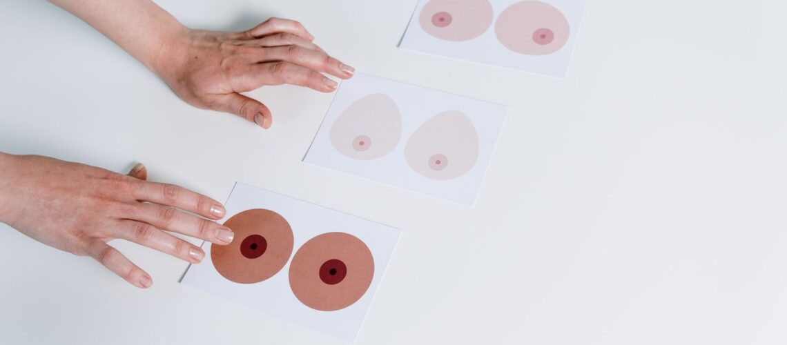 Hands arranging breast anatomy illustrations for awareness and education on a white surface.