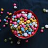 Vibrant assortment of colorful candy beans in a red ceramic bowl, perfect for sweets lovers.