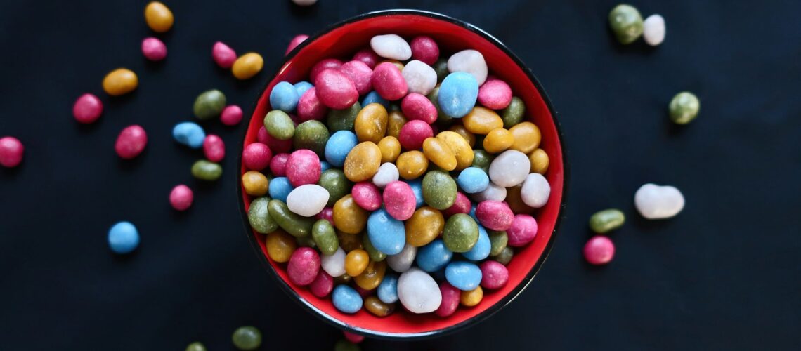 Vibrant assortment of colorful candy beans in a red ceramic bowl, perfect for sweets lovers.