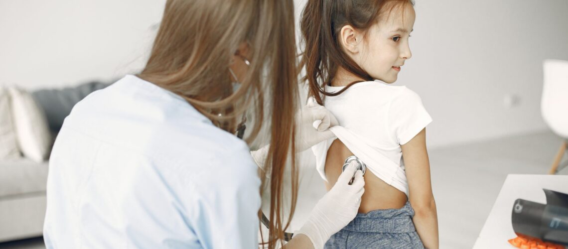 A female doctor uses a stethoscope to examine a child in a medical examination room.
