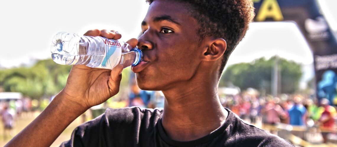 A young man drinking bottled water outdoors at a sporting event, showcasing hydration and fitness.
