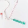 Flat lay of medical supplies with tape measure and syringe on white background, symbolizing healthcare.