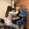 Optometrist performing an eye exam with a slit lamp in a well-lit examination room.