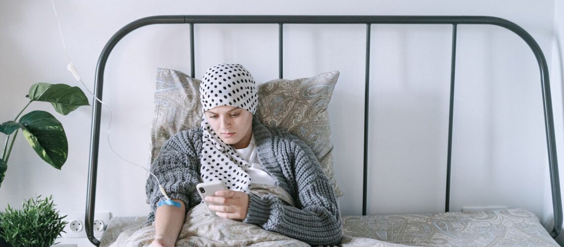 A woman undergoing chemotherapy checks her smartphone in a hospital bed, symbolizing hope and recovery.