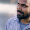 Close-up portrait of a smiling man with a beard and black hair, outdoors.