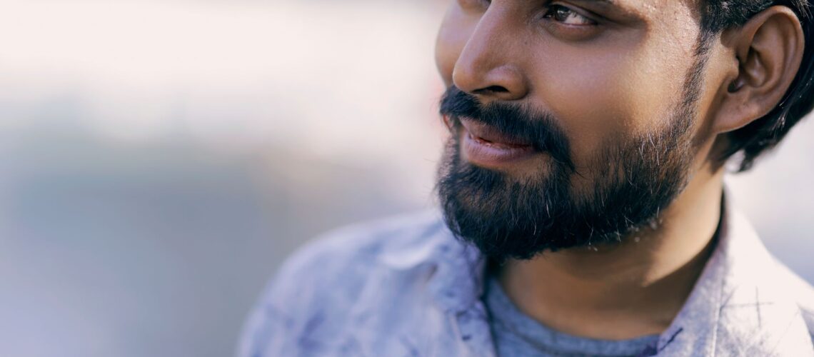 Close-up portrait of a smiling man with a beard and black hair, outdoors.