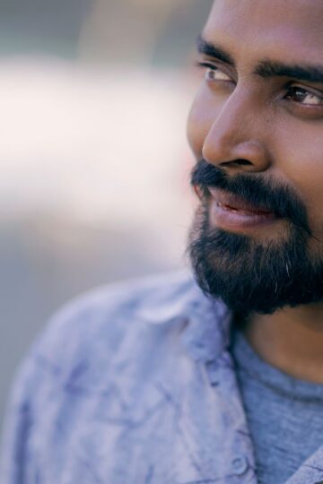 Close-up portrait of a smiling man with a beard and black hair, outdoors.