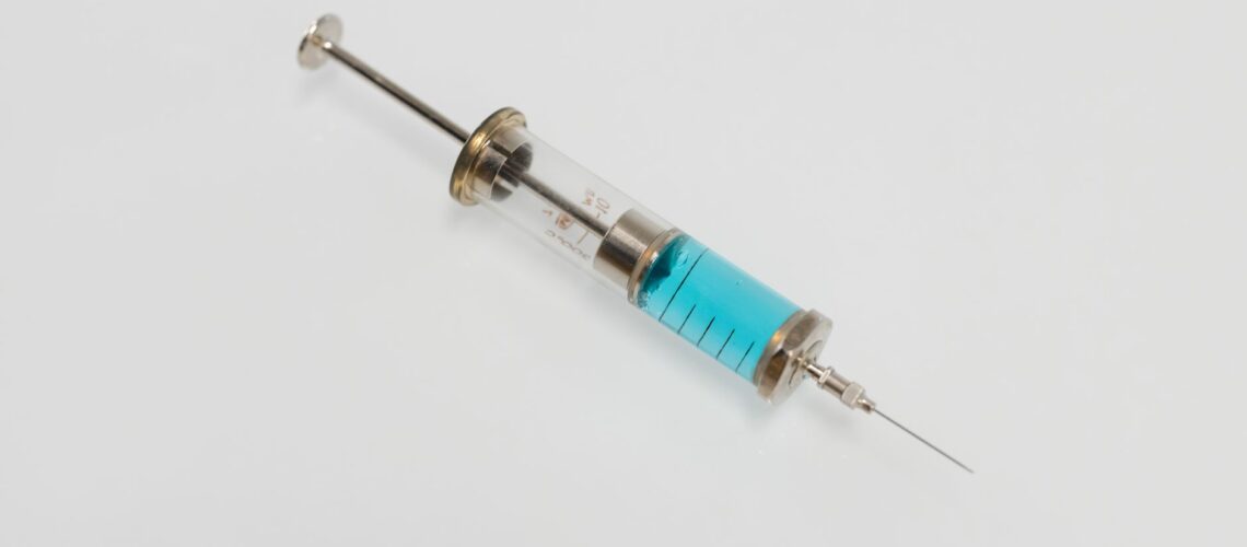 Close-up of a vintage glass syringe filled with blue liquid on a white background, minimal healthcare concept.
