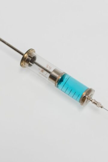 Close-up of a vintage glass syringe filled with blue liquid on a white background, minimal healthcare concept.