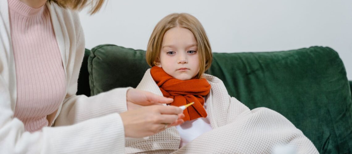 A caring moment of a woman checking a sick child's temperature on a cozy green couch indoors.