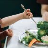 A child enthusiastically eating a plate full of fresh vegetables at the dining table.