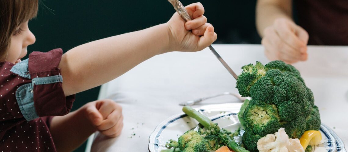 A child enthusiastically eating a plate full of fresh vegetables at the dining table.