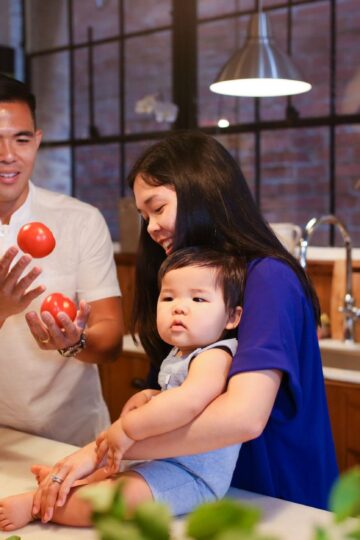 Parents and baby enjoying quality time in the kitchen with fresh vegetables.