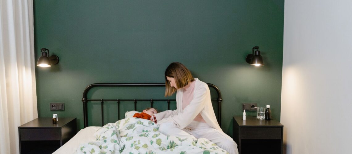A mother cares for her child with a fever in a warm, cozy bedroom setting.