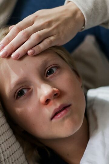Young child lying down with a hand checking for fever, indicating illness or flu symptoms.