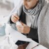 Adult male in scarf taking medicine at a desk with tissues and tablet, feeling unwell.