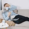 A man with a mask looks sick and checks his temperature at home.