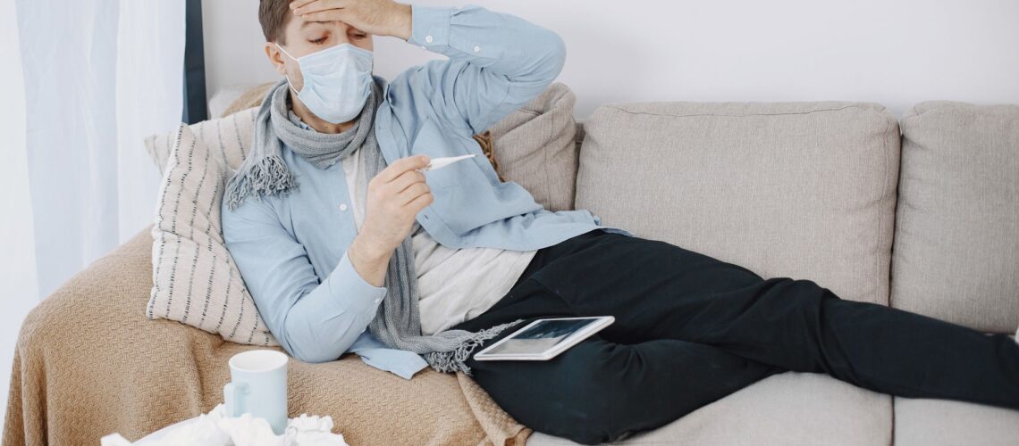 A man with a mask looks sick and checks his temperature at home.