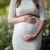A pregnant woman in a lace dress gently cradling her belly in an outdoor setting.
