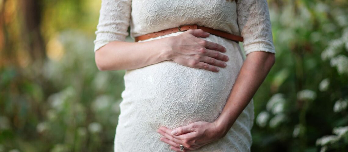 A pregnant woman in a lace dress gently cradling her belly in an outdoor setting.