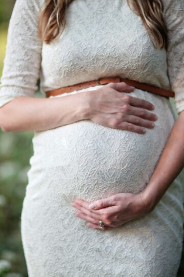 A pregnant woman in a lace dress gently cradling her belly in an outdoor setting.
