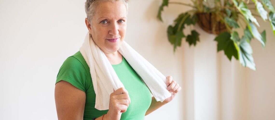 Active senior woman in green shirt with towel in home setting, promoting fitness and wellness.