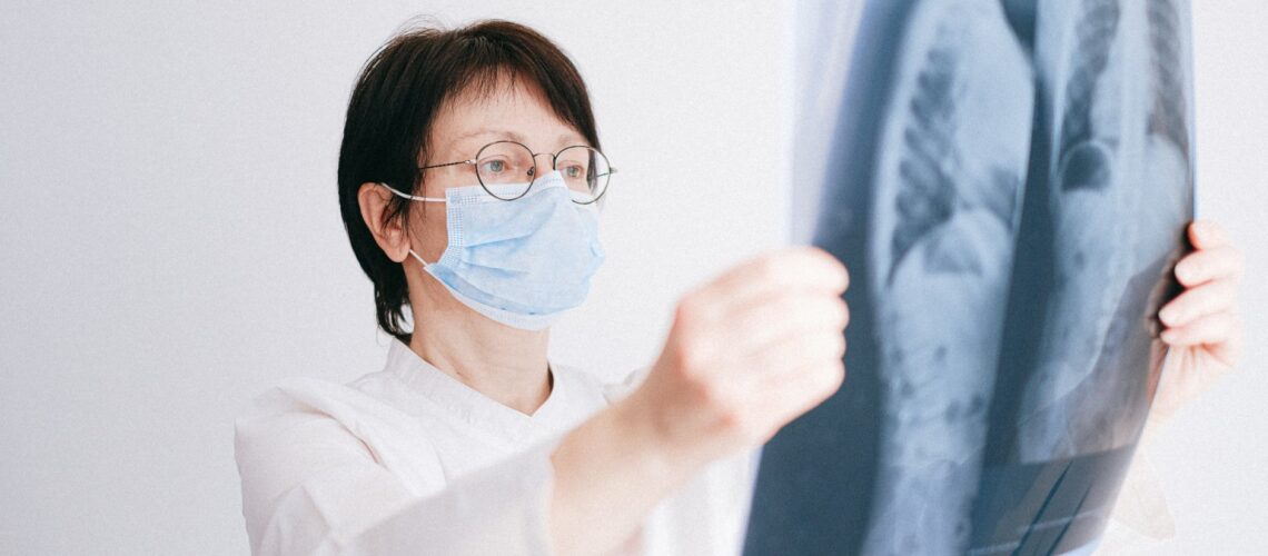 Doctor analyzes lung x-ray wearing a mask in a clinical setting.