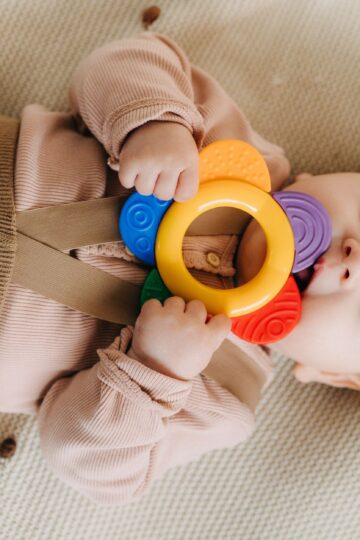 Cute baby chewing on a colorful teething toy while lying on a soft surface.