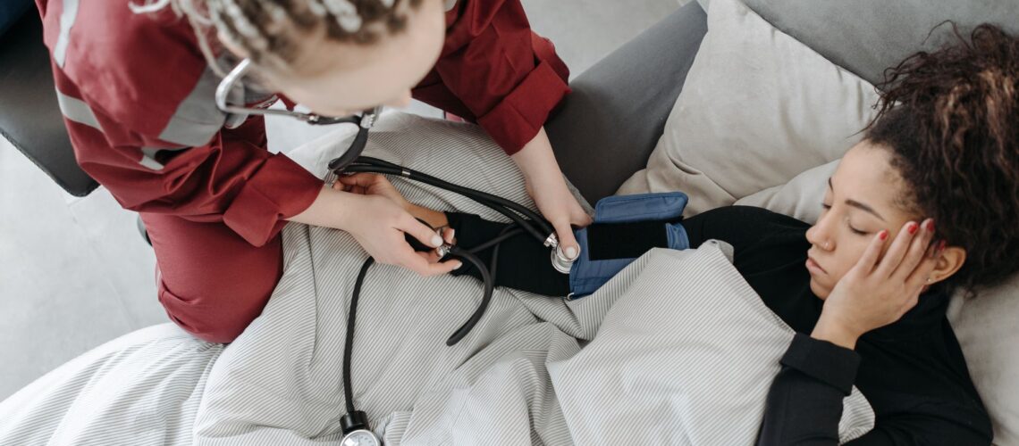 Paramedic measuring patient's blood pressure indoors, illustrating home healthcare assistance.
