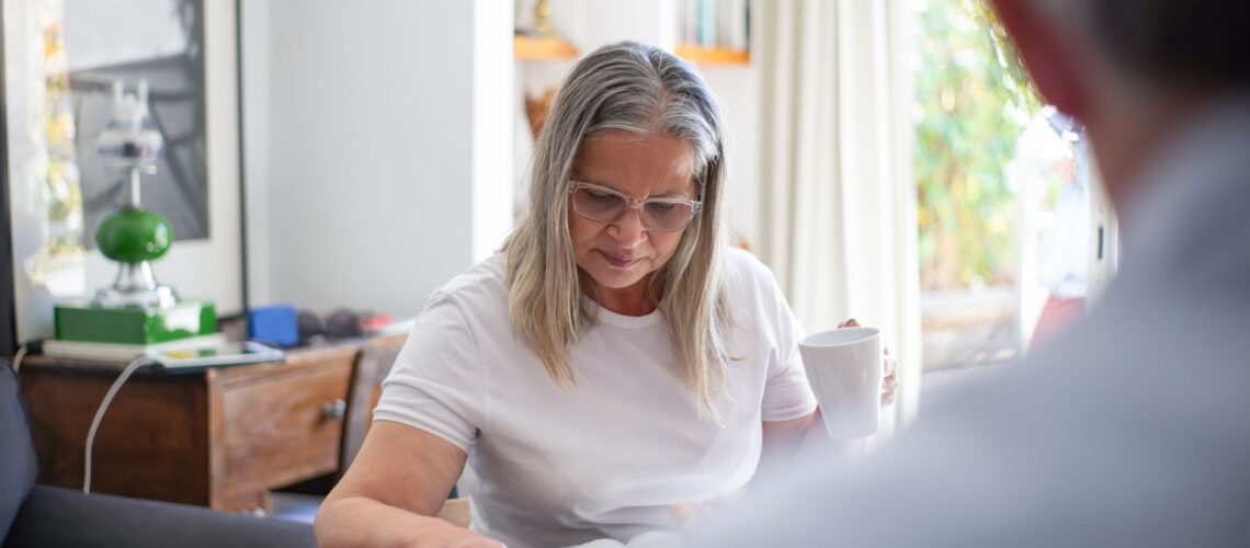 Senior woman wearing eyeglasses reading a magazine with a cup of coffee indoors.